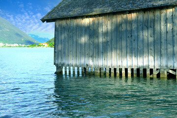 wooden hangar on water, boathouse for boats and boats on stilts, surface of mountain lake Achensee in Austria, Alps mountains in background, concept of recreation and tourism, extreme sports