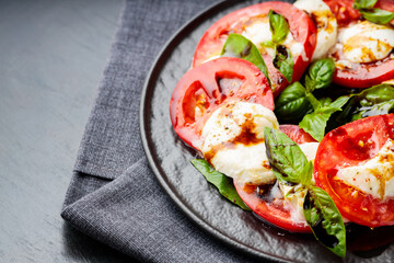 Plate of healthy classic caprese salad with ripe tomatoes and mozzarella cheese with fresh basil leaves on dark background. Close up