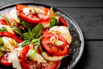 Delicious caprese salad with ripe tomatoes, mozzarella cheese and fresh basil leaves on dark wooden boards. Close up
