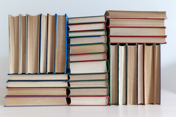 Stacks of thick old books in different bindings colors sizes lying and standing on light background