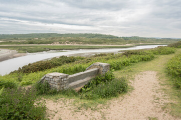 A bench, overlooking the river Ogmore in South Wales, towards the sand dunes of Merthyr Mawr. The day is cloudy.