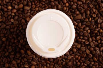 Blank disposable paper cup with plastic lid mock-up on brown background with coffee beans