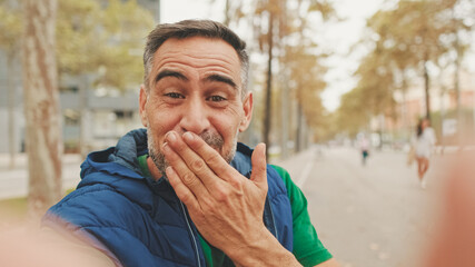 Mature man wearing casual clothes, sitting on bench in the park, talking on video call from smartphone