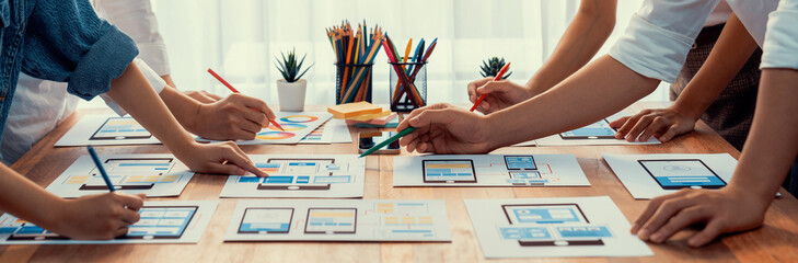 Panorama shot of front-end developer team brainstorming UI and UX designs for mobile app on paper...