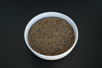 cumin seeds in a white plate on a black background