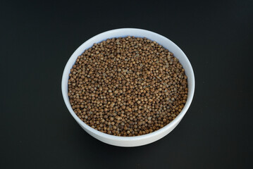 coriander seeds in a white plate on a black background