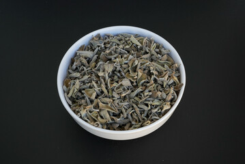 Getrocknete Salbeiblätter or Salvia officinalis  a white plate on a black background