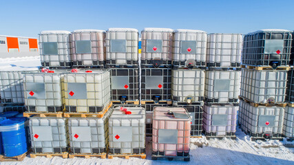 Chemical factory warehouse. Giant tanks on pallets. Square barrels for chemical liquid. Tanks with metal crate. Territory of chemical plant on winter day. Fuel tanks with flammable symbol