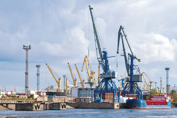Fototapeta na wymiar Sea cargo harbor. Port with cranes on shore. Harbor for loading ships. Container port on sunny day. Cargo harbor in summer weather. Export across ocean. Maritime logistics. Cargo transportation