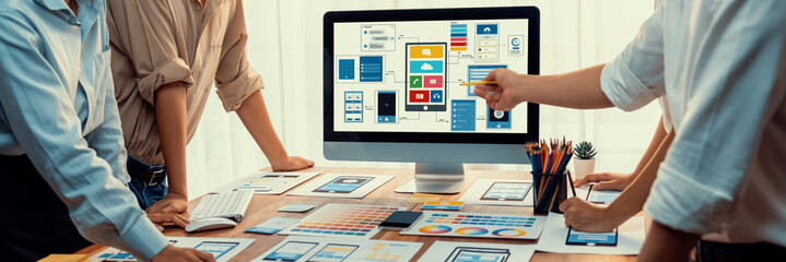 Panorama shot of front-end developer team brainstorming UI and UX designs for mobile app on laptop...