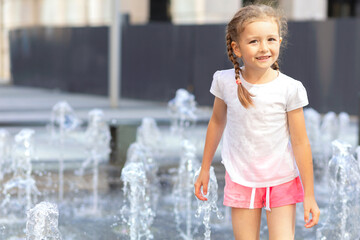 Active little girl playing with splash spray water. Happy kid in fountain in wet clothes. summer children pastime, entertainment, recreation. child's leisure, childhood in city