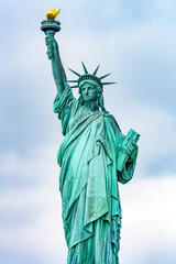 Fototapeta premium New York, New York, United States. August 07, 2023. Dramatic and detailed image of the Statue of Liberty with strong shades of green, sky with many clouds and very high resolution.