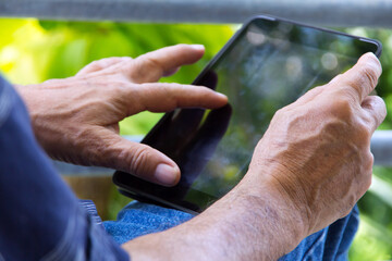 Senior man sitting outside reading E-book on his tablet.