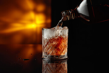 Pouring whiskey from a bottle into a glass with ice.