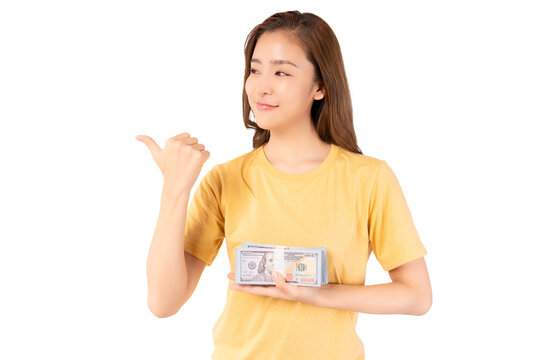 Happy young asian woman holding money dollars banknotes and pointing to space isolated over yellow background Happy asian lady hold money dollars and Smiling girl earning a lot of money or win lottery