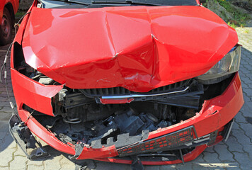 Crashed car of red color. Front view of the wrecked vehicle. The car crash. Abandoned passenger car is completely broken. Traffic accident. Destroyed in an accident expensive car