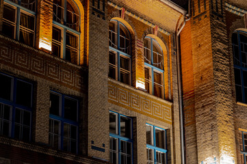 Obraz premium Old house in europe Night photo of old city landmark, long explosure warm light trails. Bricks wall old architecture, illuminated wall