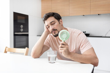 Tired and overheated man suffering from a heat attack uses an electric handy fan to cool himself down in a hot summer day © Vitaliy