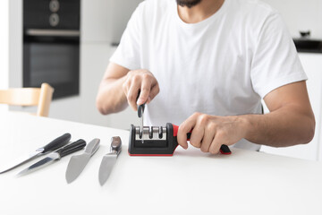 Close-up photo of man sharpening knives with special knife sharpener at home	