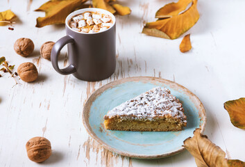 Top view of female hands holding marshmallows on shabby table with piece of cake, walnuts and scattered leaves, autumn composition