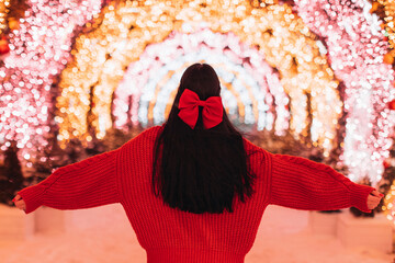 Back view brunette woman in a knitted cozy red sweater and a bow in her long hair against the...