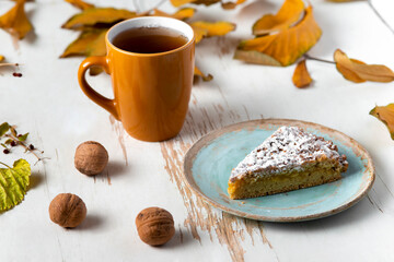 Baked pie served with hot tea on table with dried leaves and walnuts .autumn composition