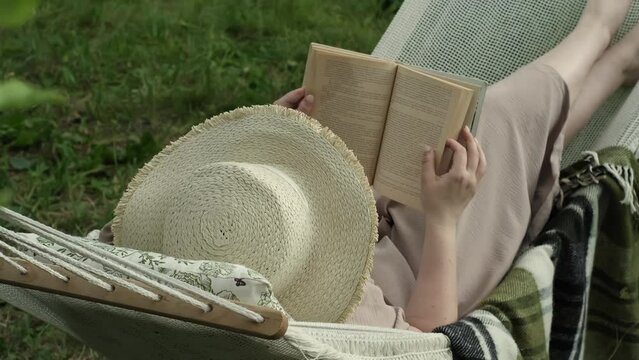 Mental wellness takes spotlight as woman indulges in dual therapy of literature and nature, reading peacefully on hammock in her garden. concept of self-care, need for personal time and space.