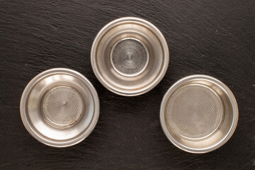 Three metal sieves for a coffee maker on a slate stone, macro, top view.