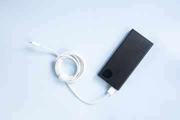 A smartphone charging with black power bank on blue background. Top view with copy space.