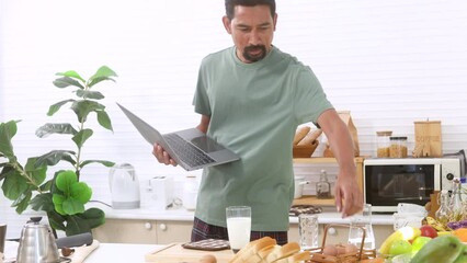 4k, candid busy Asian businessman holds laptop hungry takes a glass of milk for breakfast in kitchen hurry goes back to home office continue working, lifestyle Hispanic male freelance time management - Powered by Adobe