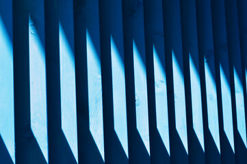 Beautiful wooden blue slats. A streak of sunlight on a wooden fence. Bright abstract background. Element of finishing the facade of the building.