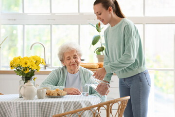 Young woman pouring water into glass for her grandmother in kitchen