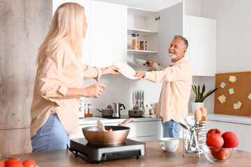 Mature man giving plates to his wife in kitchen