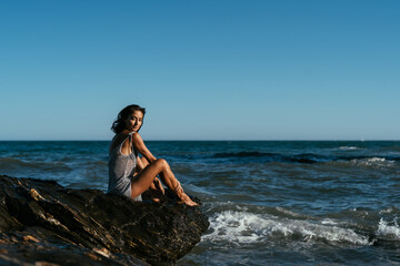 beautiful brunette girl in a silvery net stands on the stones on the seashore