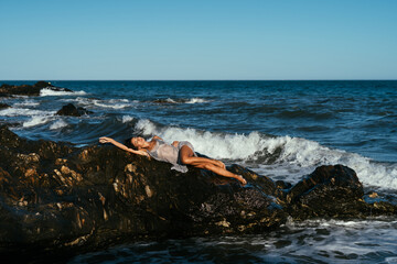 beautiful brunette girl in a silvery net stands on the stones on the seashore