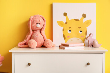 White chest of drawers with toys in children's room near yellow wall