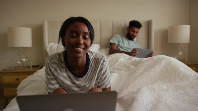 Couple at home in bed with woman using laptop and man on digital tablet - shot in slow motion