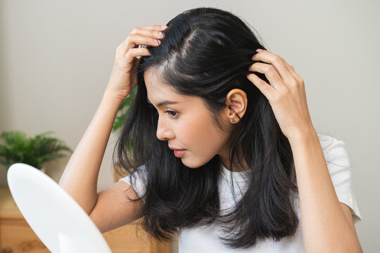 Damaged hair symptom, problem hair fall asian young woman, girl worry about balding, looking at scalp in mirror, hand in break into front hair loss, thin problem. Health care treatment for beauty.