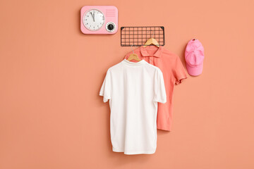 Stylish t-shirts and cap hanging on pink background
