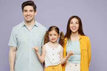 Fototapeta premium Young sad fun parents mom dad with child kid daughter girl 6 years old wear blue yellow casual clothes point thumb fingers on father and mother isolated on plain purple background. Family day concept.