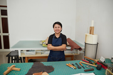 Young Asian female leather worker standing in her studio