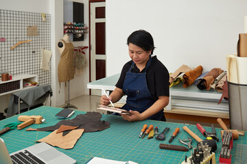 Asian female leather worker sketching on a digital tablet using digital pen