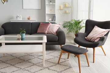 Interior of light living room with grey armchair, footstool and sofa