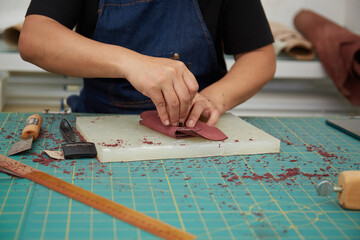 Hand close up of Asian Female leather worker working with tool and a piece of leather 