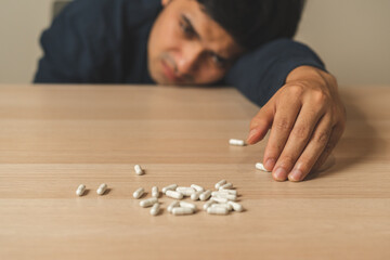 Stressed, sad asian young man, male take medicine, lying on table. Close up hand of abuse overdose...