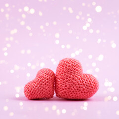 Two knitted pink hearts on a purple background with golden lights and with a place for your text. Symbol of love, happiness, joy and loyalty.