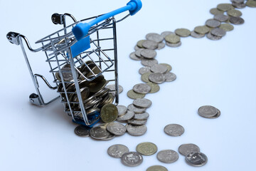Supermarket trolley with scattered coins on a white background.