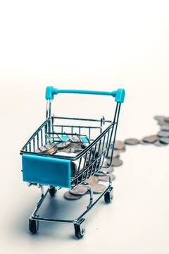 Supermarket trolley with scattered coins on a white background.