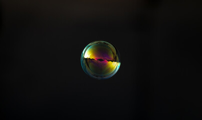 Cyan gold soap bubble on blurred dark background. Close-up.