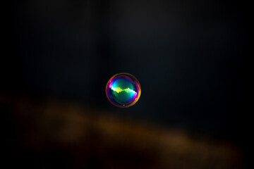 Colorful gold soap bubble on blurred dark background. Close-up.